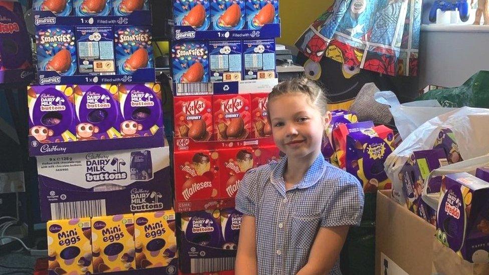 Ellie in her school uniform surrounded by stacks of Easter eggs in their boxes