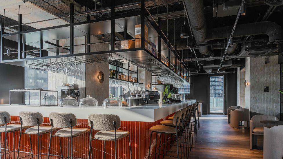 A plush, modern bar/lounge, with various stools  at the bar and seats just off it. 