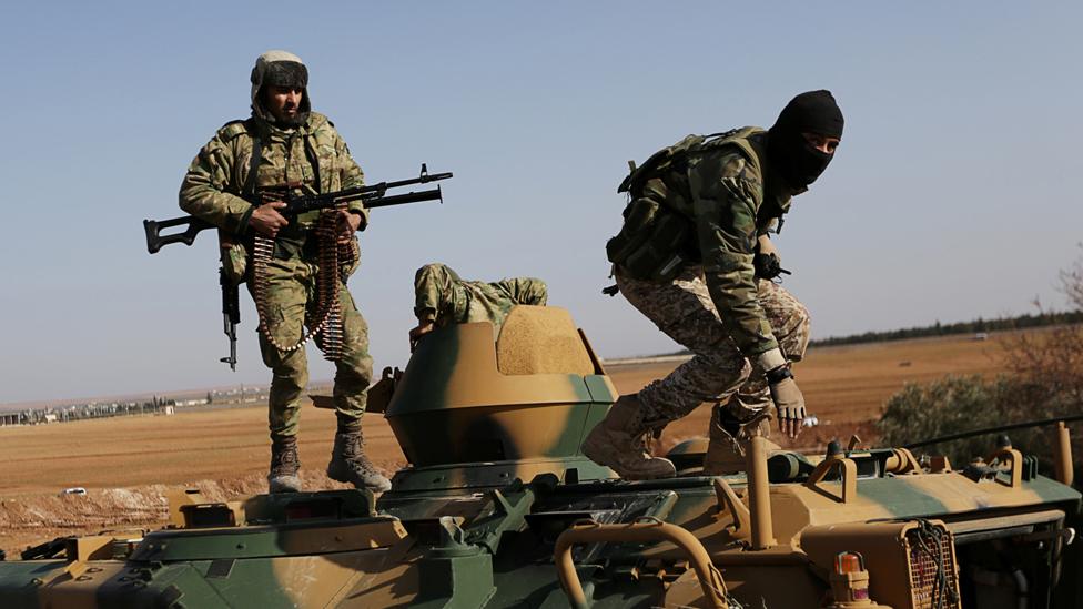 Rebel fighters stand with their weapons on a military vehicle as they head towards the northern Syrian town of al-Bab