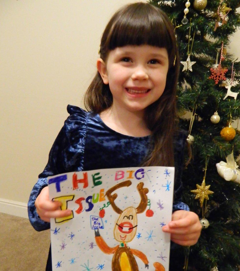 Evelyn Weston holding her drawing while standing next to a Christmas tree