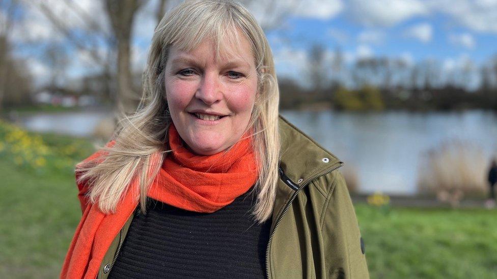 A woman by a pond in an orange scarf