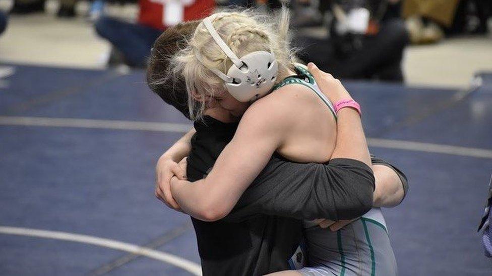 A teenage girl dressed in amateur wrestling gear hugging an older man