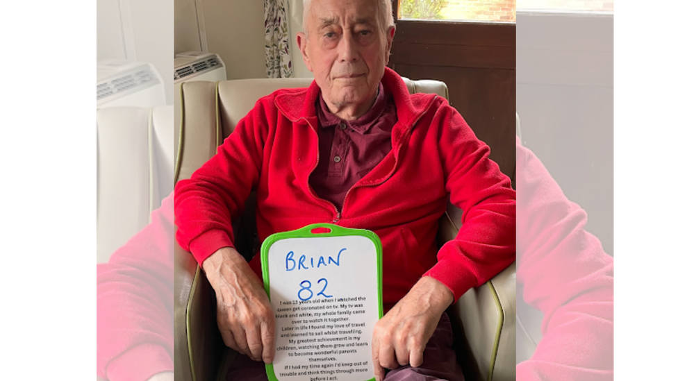 Brian wearing a bright red jumper while holding his personal message.