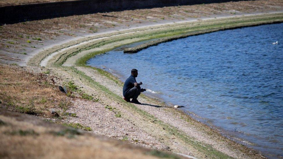 A person sits by a water reservoir with low water levels and dried grass at Walthamstow Wetlands in London, Britain, 10 August 2022