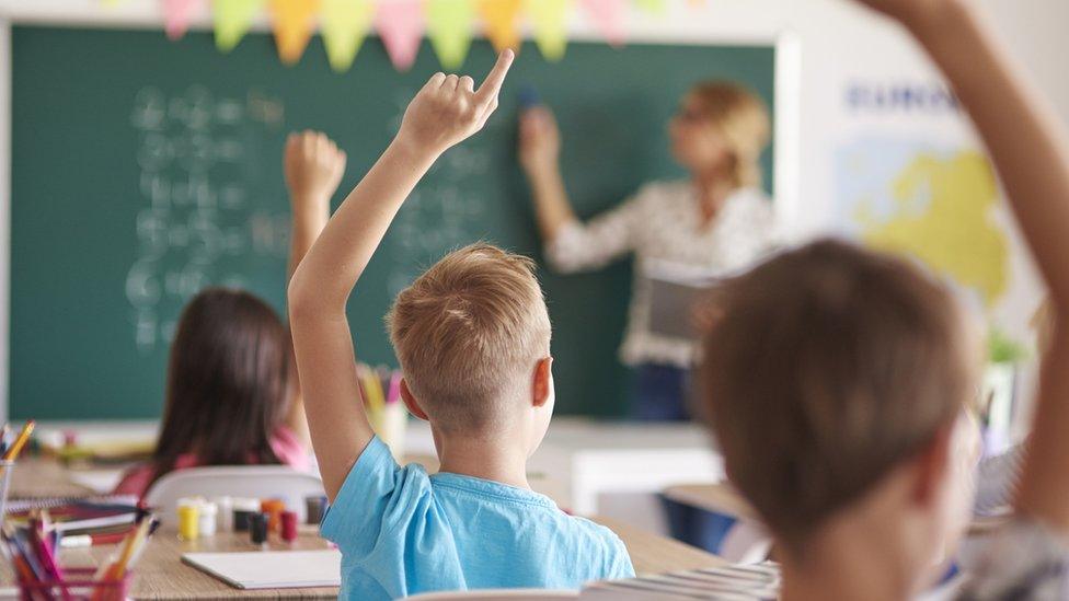 children raising hands in a classroom