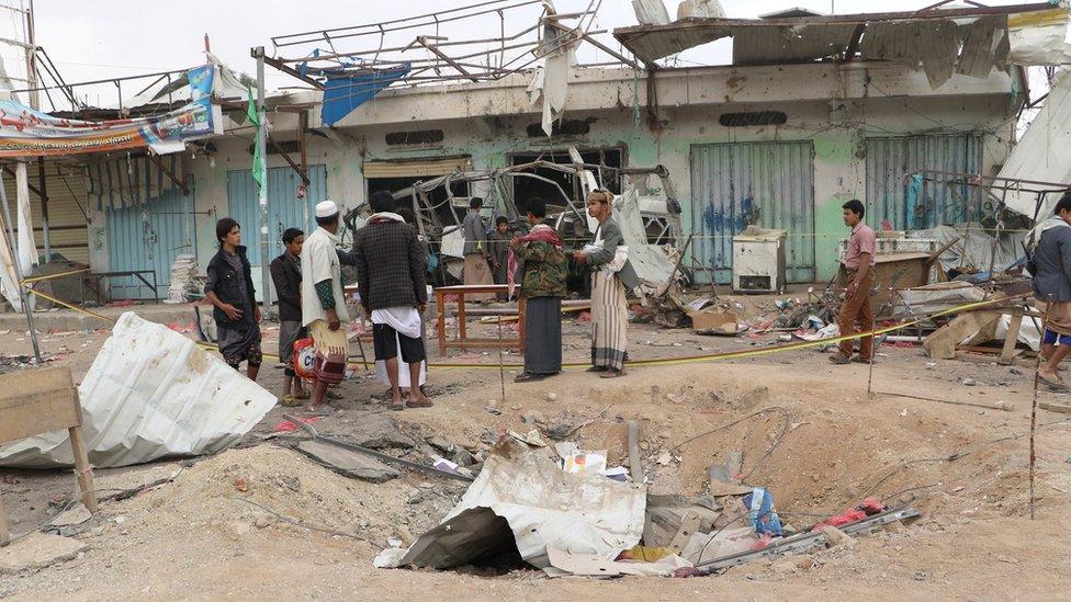 People stand at the site of an air strike on a bus in Dahyan, Saada province, Yemen (10 August 2018)