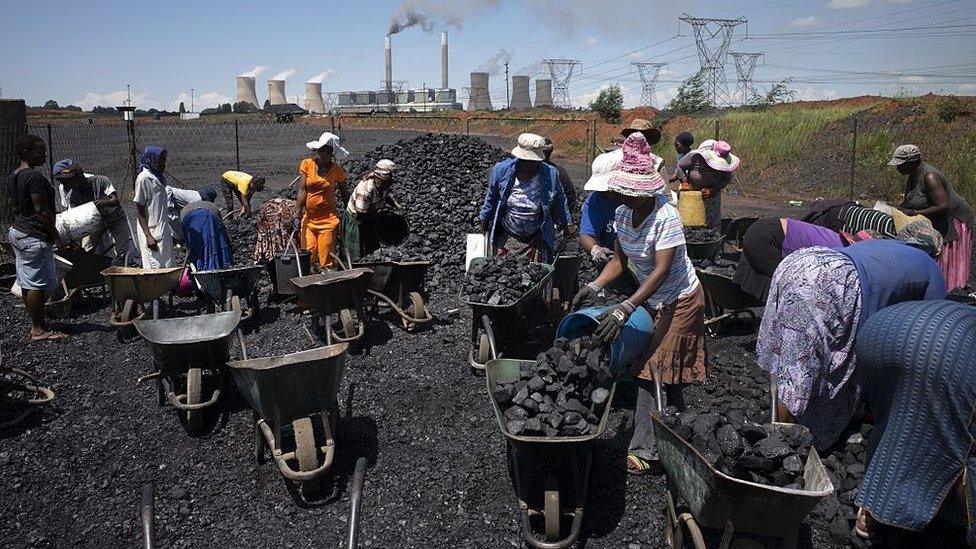 Women from the coal-dust covered and power-line pollution-exposed Masakhane settlement fill their wheel barrows for a load of free coal provided by a nearby mine on February 5, 2015 in Emalahleni