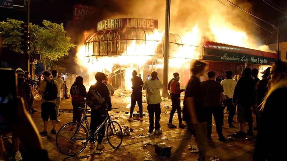 Protesters gather to watch a liquor store burning