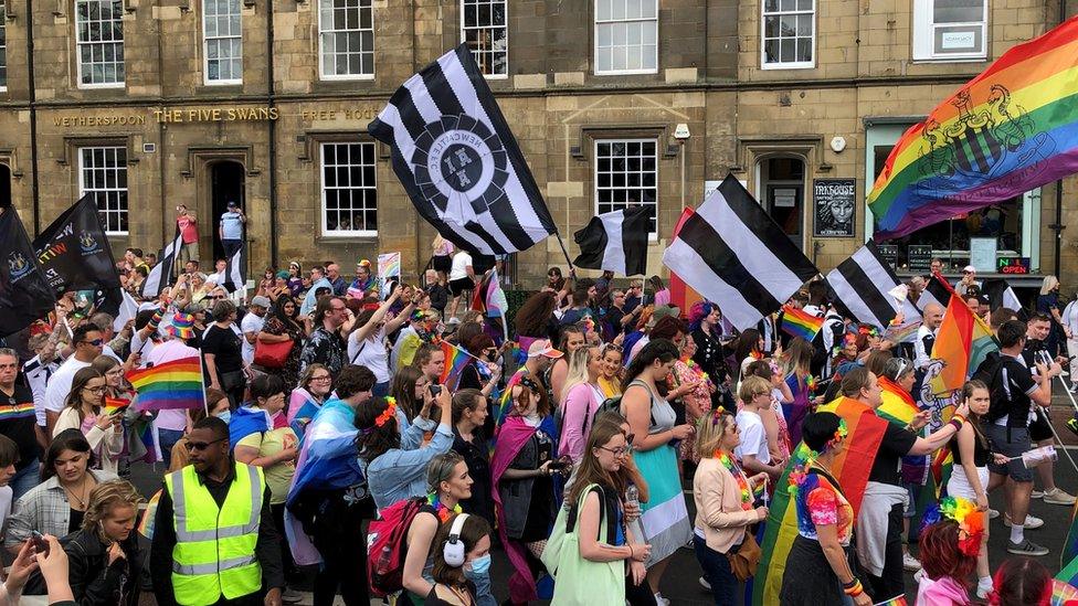 People carrying flags including Newcastle United and rainbow motifs parade down street