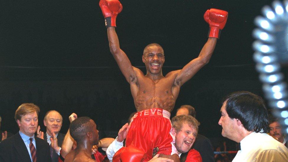 Boxer Steve Robinson smiles and has his arms in the air as he his lifted high by one of his trainers.