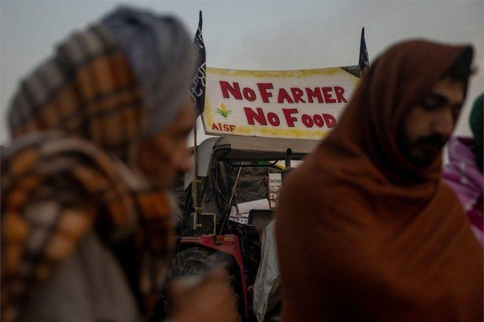 Farmers stand next to a fire as they warm themselves on a cold winter morning at the site of a protest against new farm laws, at Singhu border, near New Delhi, India, DecemberIMAGE COPYRIGHTREUTERS