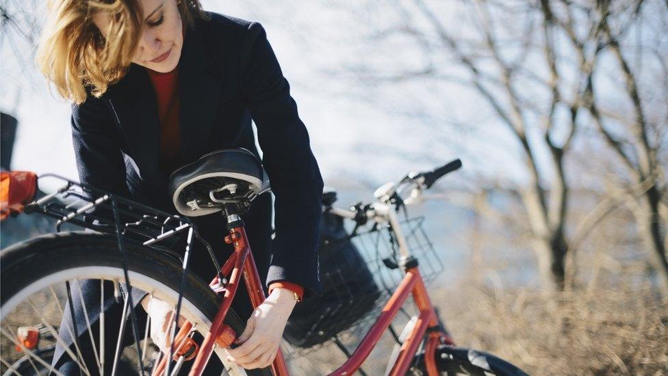 Woman bending while locking bicycle on sunny day during winter - stock photo