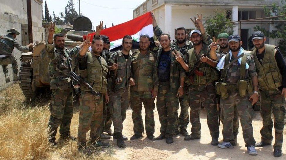 Soldiers loyal to the Syrian regime pose for a photograph as they gesture and hold the national flag in the village of Debaa near Qusair (June 2013)