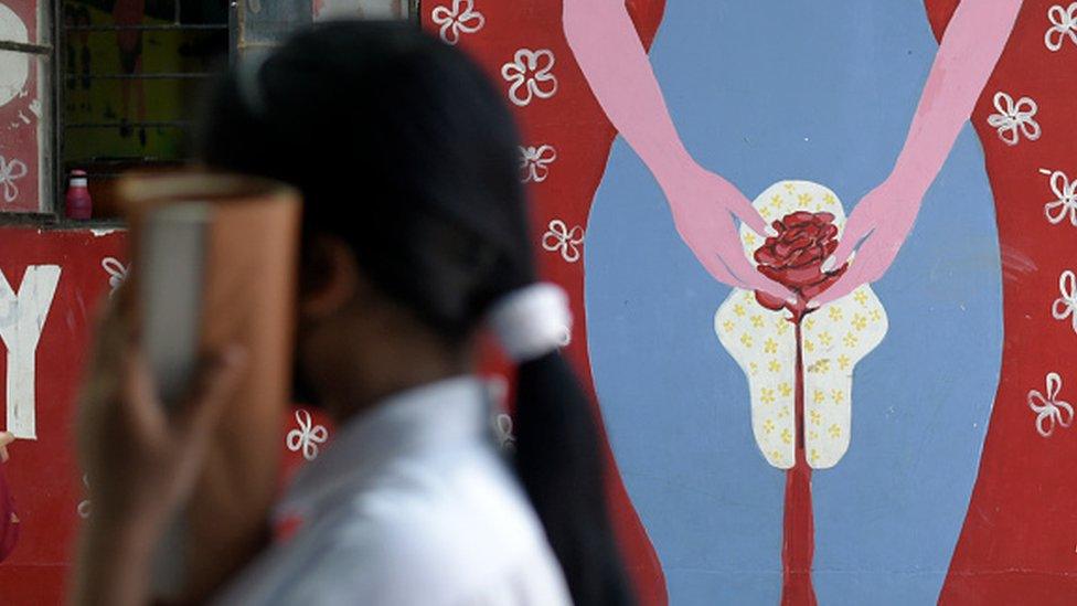 A girl in front of a wall painting about female menstruation