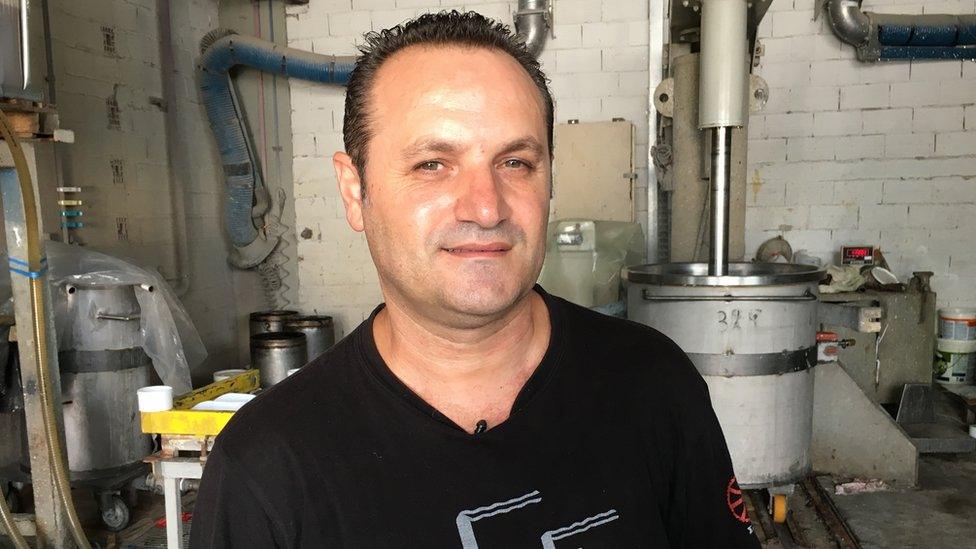 Dimitris Koumatsioulis is pictured in a factory setting, with industrial drums visible in the background