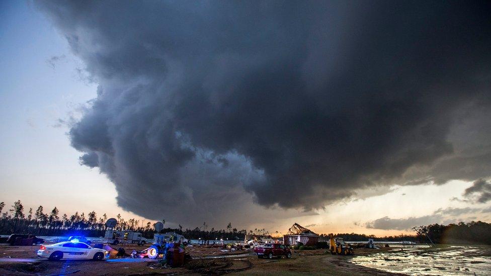 Storm clouds approach emergency crews at the scene of a house cut in half by a tornado near where seven people were killed outside Adel, Georgia