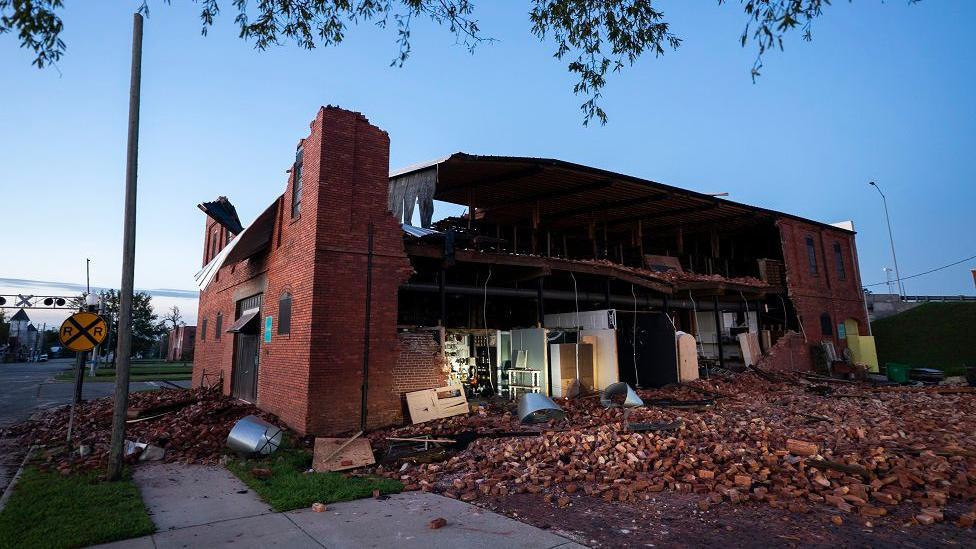 A house is pictured with one side ripped of, with piles of bricks next to it