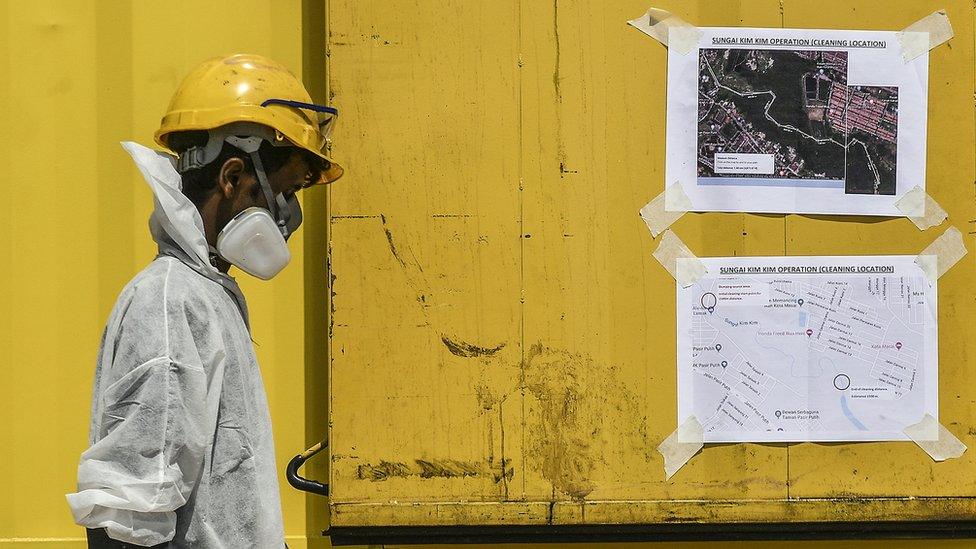 An emergency worker passes by maps displaying cleaning locations of the site