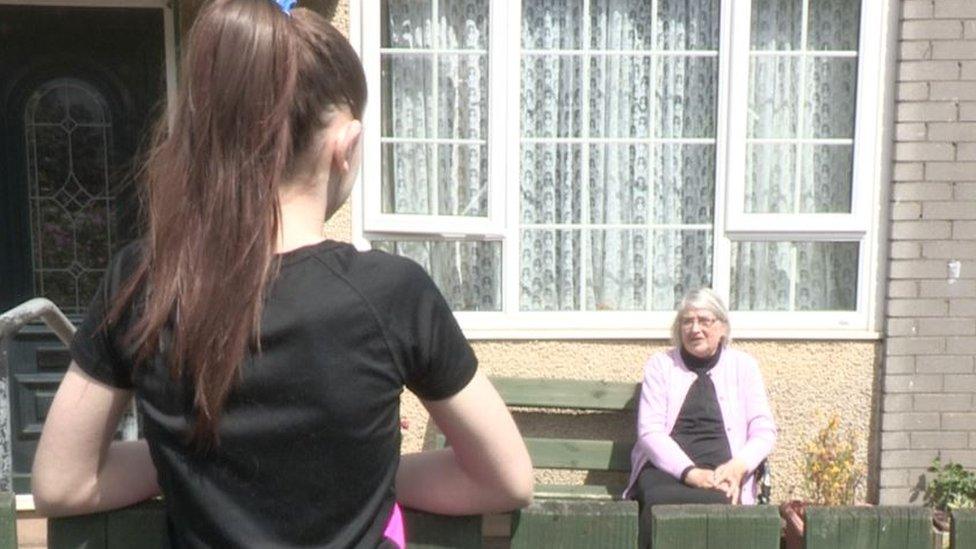 Patsy McGrail sitting on a bench, with granddaughter Anna looking on from a fence