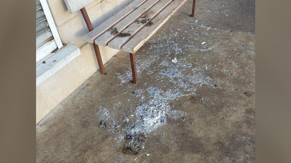 Vandalism at a park bench where a deodorant can has been set on fire. Ash remains on the floor and parts of the bench has been burnt.