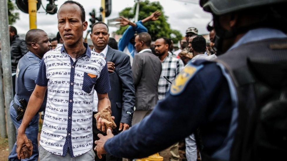 Somali immigrant armed with a rock is blocked by a police officer