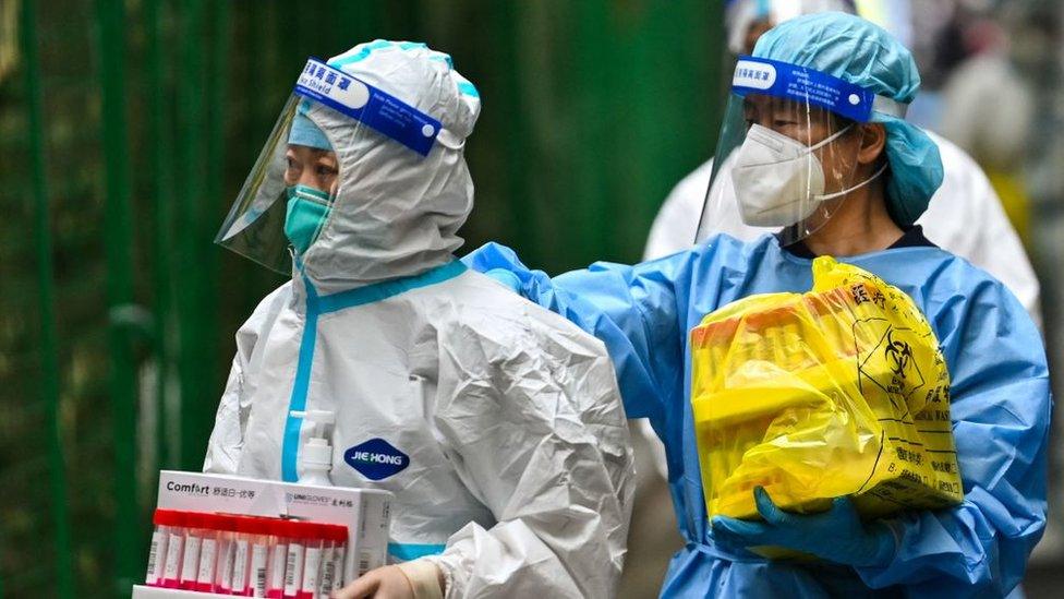 Health workers walk holding swab samples taken from people next to the entrance of a residential area under Covid-19 lockdown in the Xuhui district of Shanghai.