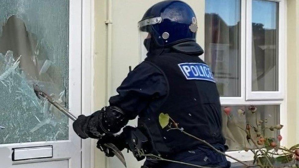 A police officer smashing in a glass panel on a door