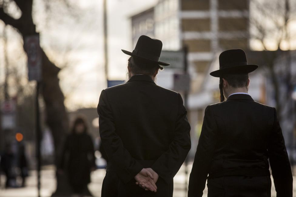 Two Jewish men, photographed from behind, walking along a street in London's Stamford Hill area