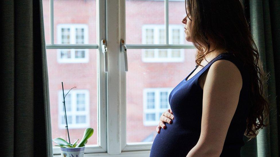 Expectant woman looking out of her window