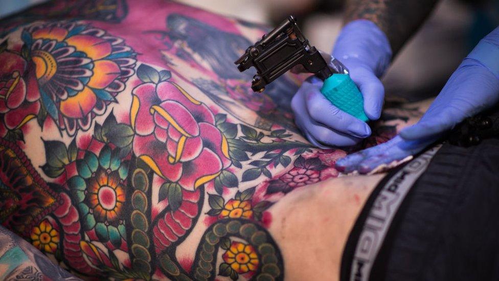 A close-up file photo from 2017 tattoo convention shoes someone having colour applied to large floral back tattoo