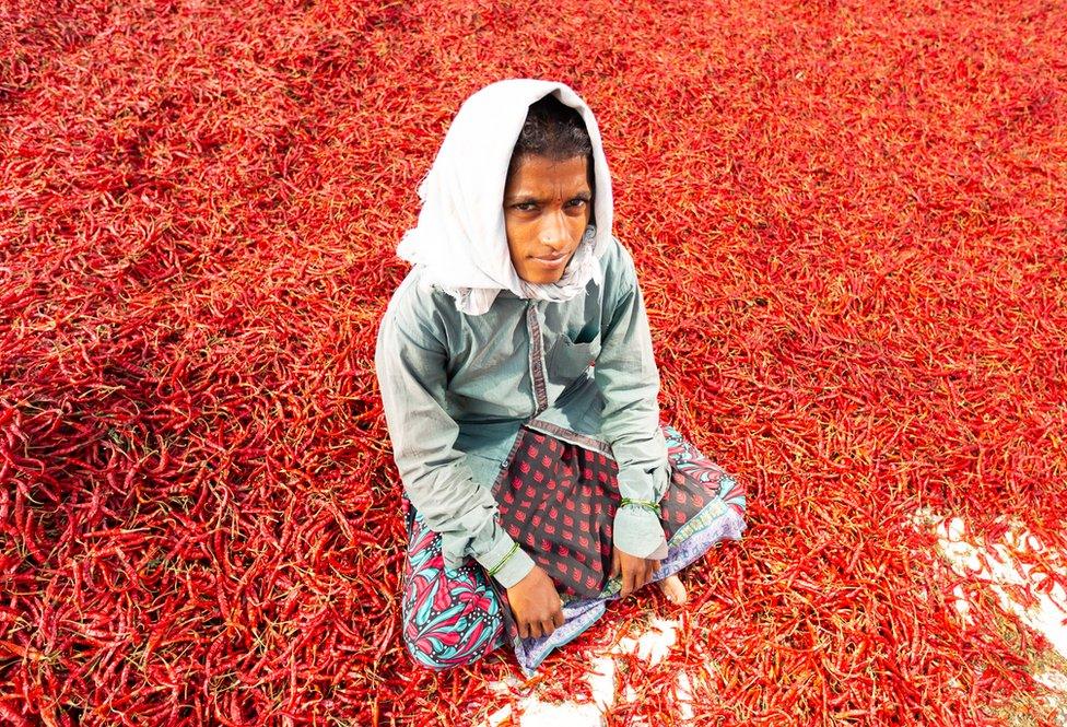 A girl sits on the ground covered in red chillies