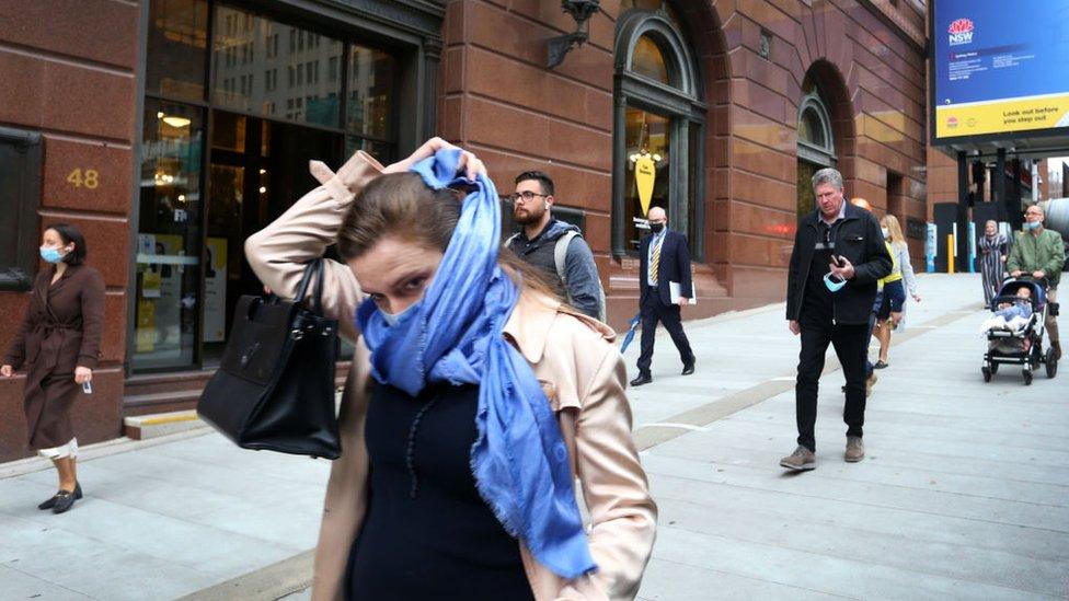 A woman walking through Sydney's city centre wraps a scarf around her face