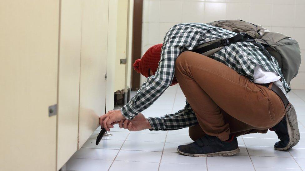 A man takes a photo under a toilet door - stock photo