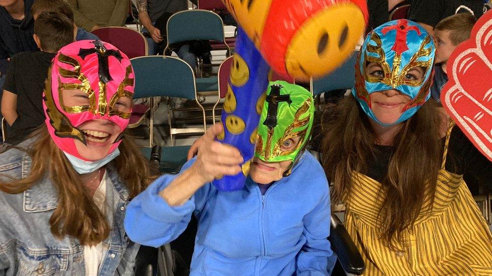 Photograph of Jane in a wrestling mask with a blow up hammer, alongside Imogen Spencer, Wellbeing Assistant on the left, and Sabina Green, Wellbeing Coordinator on the right