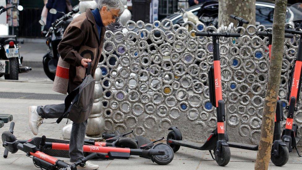 A pedestrian steps over Voi's e-scooters in Paris