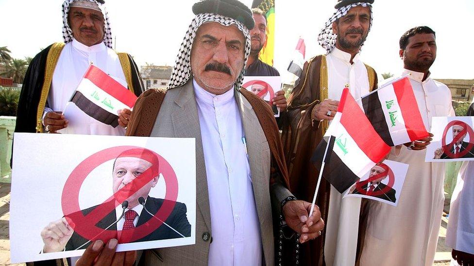 Iraqi tribesmen hold national flags and posters bearing a portrait of Turkish President Recep Tayyip Erdogan crossed out during a protest against the continued presence of Turkish troops in northern Iraq