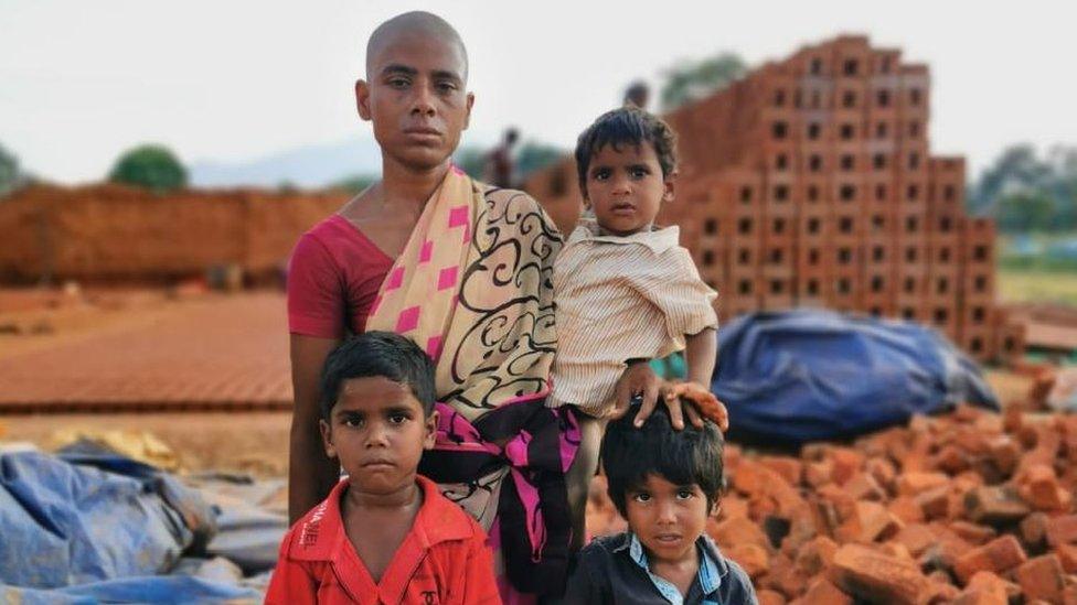 Prema standing in front of a brick kiln with her three sons