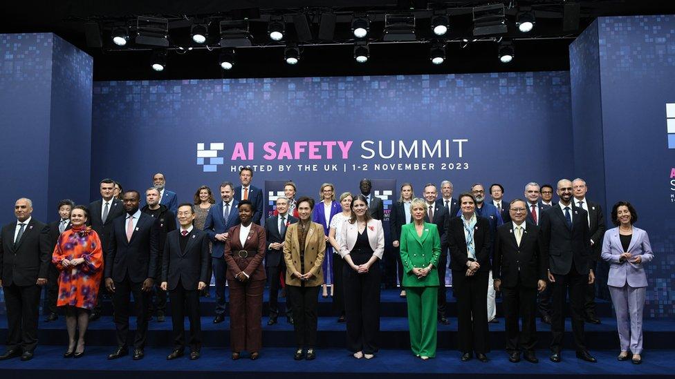 international ministers stand together in front of a sign that reads ai safety summit