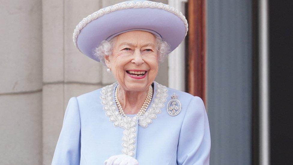 queen smiling wearing a light purple suit and pearls