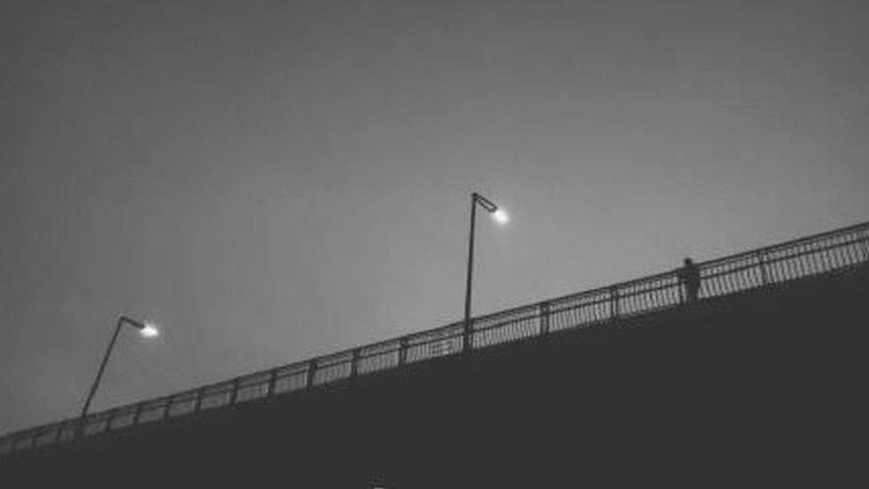 A figure stands alone on a bridge