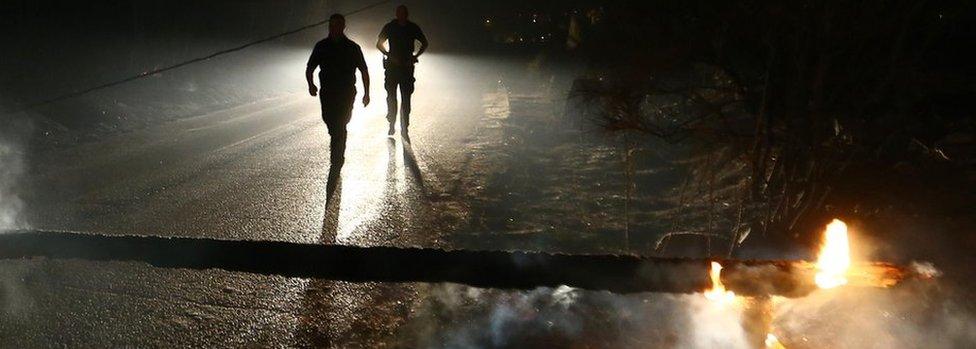 Local residents walk on the blocked road by timber, burned by wildfire in the village of Mravince, Split