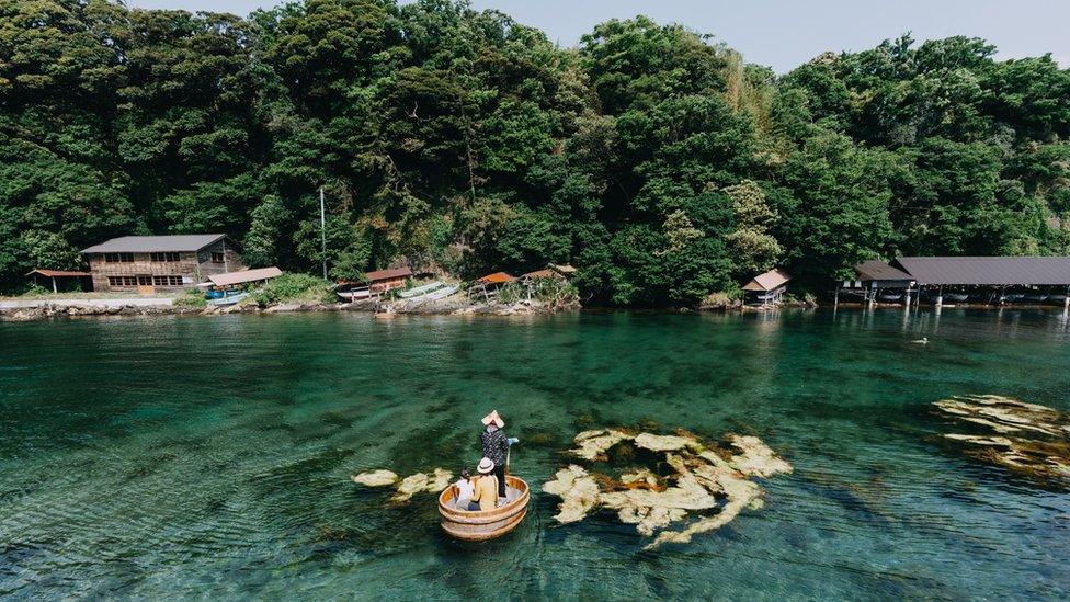 a fishing boat off the coast of an island full of trees floating between rocks in the sea