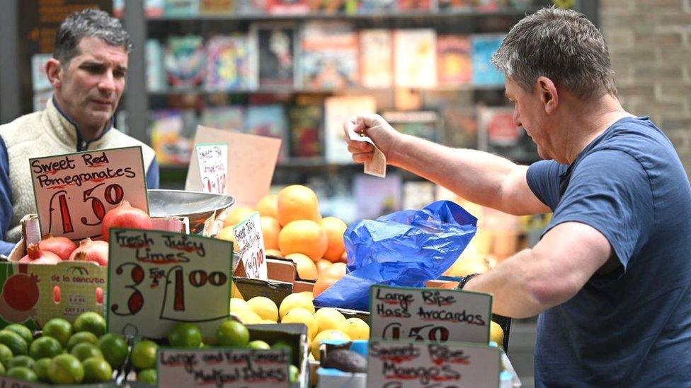 A customer pays for fruit and vegetables with a £10 note at a market stall in London