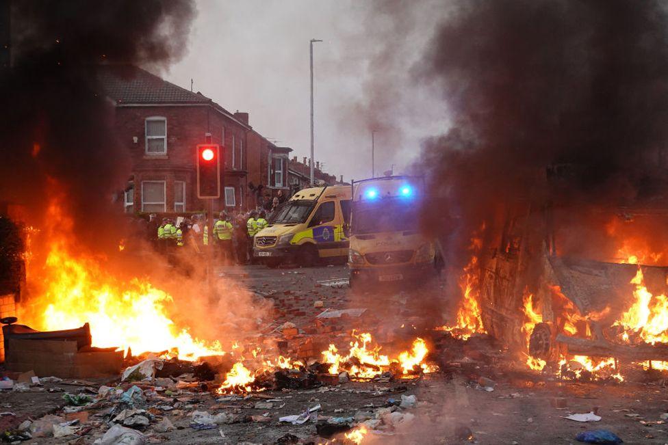 Riot police hold back protesters near a burning police vehicle after disorder broke out in Southport, England. 