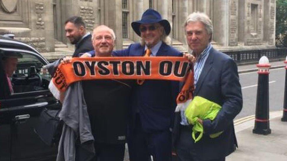 Owen Oyston (centre) poses outside the court with a protestor holding an "Oyston Out" Blackpool scarf