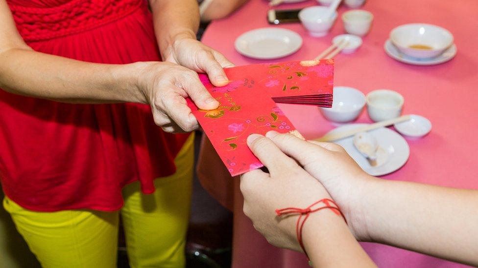 A woman hands over two red envelopes