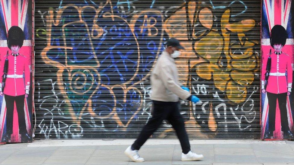 Man wearing face mask walking past closed shop shutters