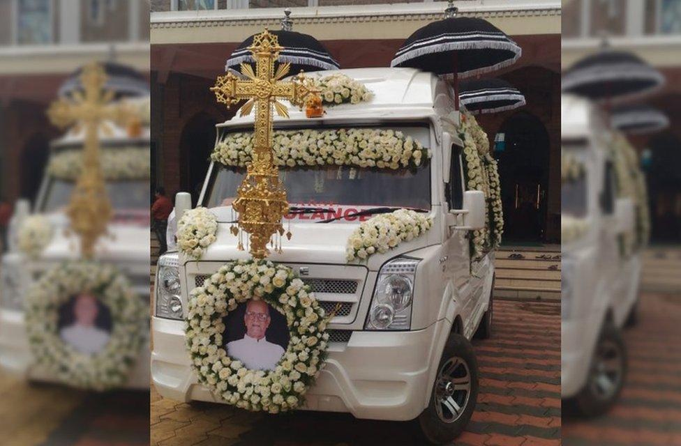 An ambulance decked with flowers and black umbrellas