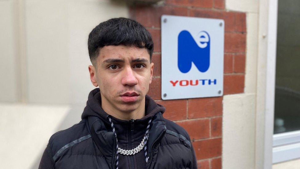 A young man stands in front of a sign for NE Youth