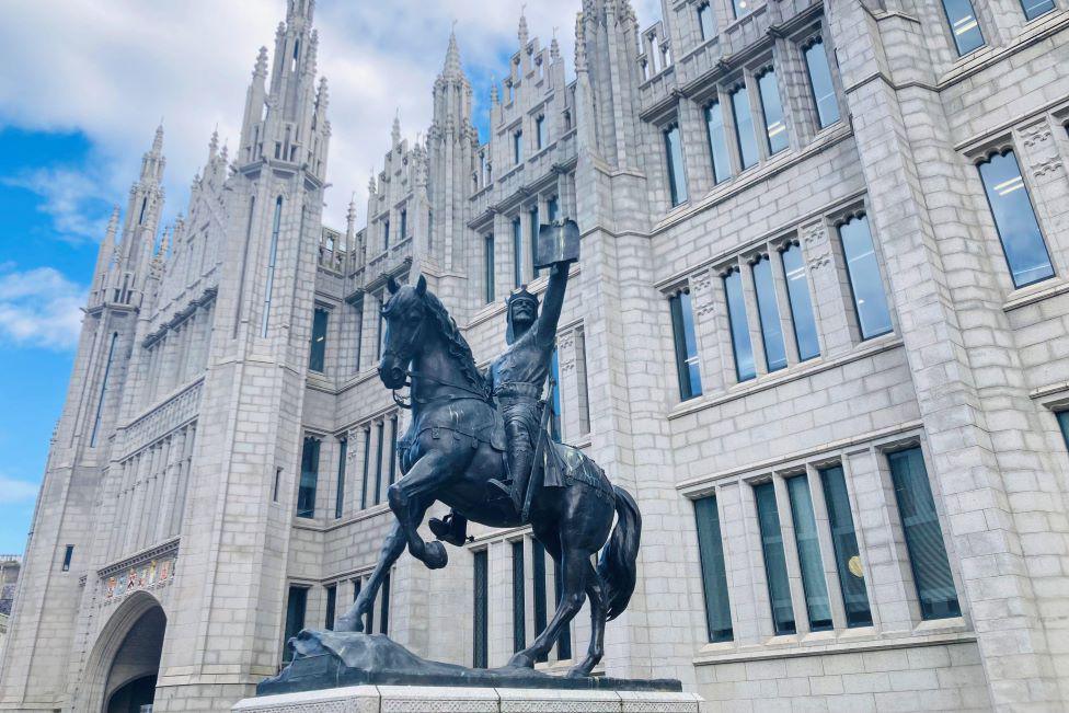 Statue of man on horseback outside an impressive granite building.